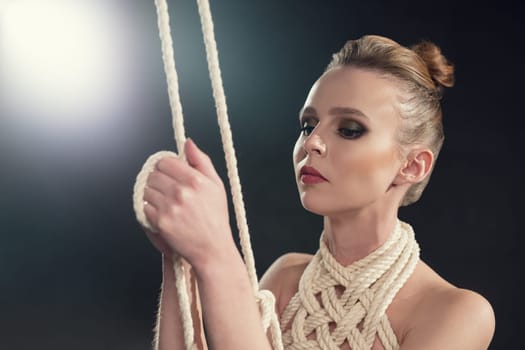 Beautiful naked woman tied up with rope portrait against black wall