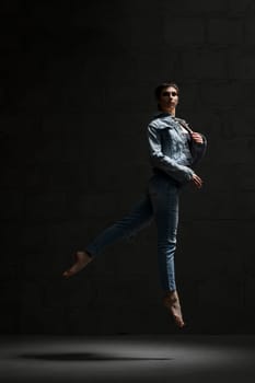 Ballet dancer with shot haircut in jeanswear jumping gracefully in dark room
