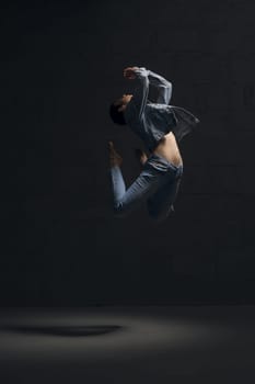 Girl with shot haircut in jeanswear dancing gracefully in dark room full-length shot