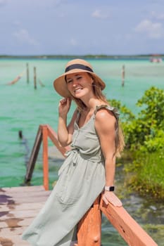 Female tourist in a turquoise dress standing on a wooden pier over the turquoise waters of Bacalar Lake, Mexico. Peaceful tropical travel destination concept.