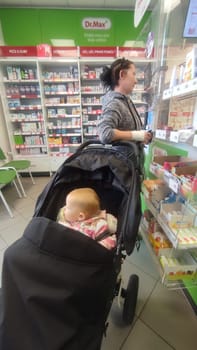 October 22 2024 Hradec Kralove, Czech Republic Europe, Kralov region, baby with pacifier sits in black stroller, child in pharmacy, medicines on shelf High quality photo