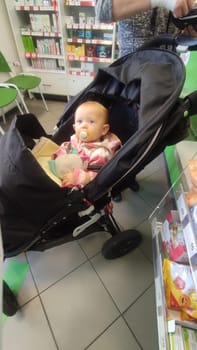 October 22 2024 Hradec Kralove, Czech Republic Europe, Kralov region, baby with pacifier sits in black stroller, child in pharmacy, medicines on shelf High quality photo