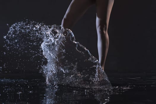 Barefoot slender woman dancing in water in dark room cropped shot