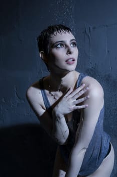 Woman in wet t-shirt standing under water in dark room portrait