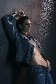 Brunette in wet jeans shirt and jeans standing under water in dark room profile portrait