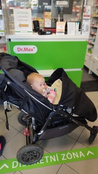 October 22 2024 Hradec Kralove, Czech Republic Europe, Kralov region, baby with pacifier sits in black stroller, child in pharmacy, medicines on shelf High quality photo
