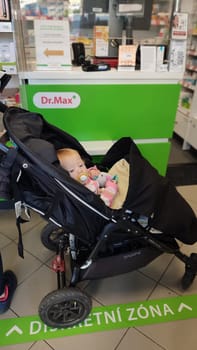 October 22 2024 Hradec Kralove, Czech Republic Europe, Kralov region, baby with pacifier sits in black stroller, child in pharmacy, medicines on shelf High quality photo