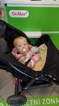 October 22 2024 Hradec Kralove, Czech Republic Europe, Kralov region, baby with pacifier sits in black stroller, child in pharmacy, medicines on shelf High quality photo