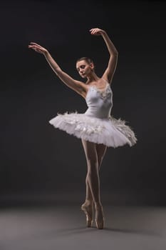 Ballerina in tutu and pointe dancing gracefully in dark room full-length shot