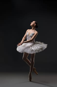 Ballerina wearing white tutu dancing on pointe view in the dark room