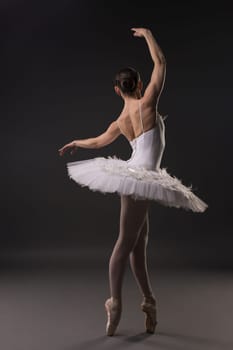 Ballerina in tutu and pointe dancing gracefully in dark room rearview