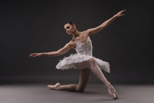 Ballerina in tutu and pointe in a gracefull pose in dark room full-length view