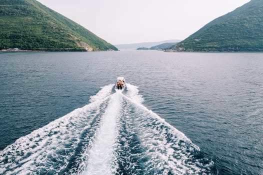 White motor yacht sails across the sea towards a green mountain range. Back view. Drone. High quality photo