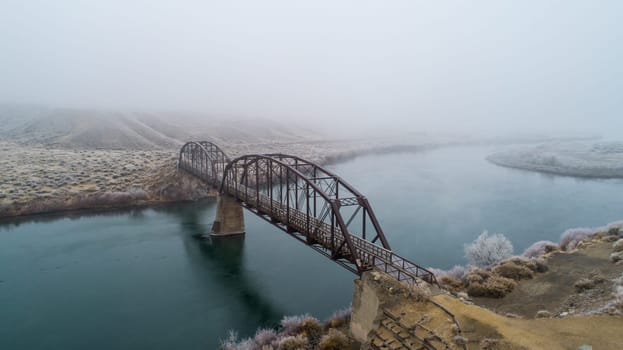 A captivating bridge spans a tranquil river, enveloped in a serene morning mist, creating a dreamy and atmospheric rural landscape scene in guffy Idaho near celebration park