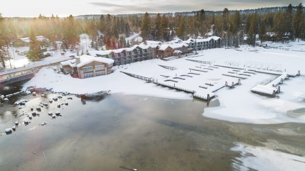 A serene winter scene of a lakeside lodge surrounded by snow-covered cabins and trees, capturing the peaceful essence of a snowy retreat in nature.