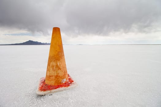An orange traffic cone stands alone on an expansive salt flat. The scene captures isolation, tranquility, and the unusual contrast between the vibrant cone and the muted landscape.