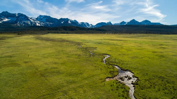 An expansive aerial shot of a lush green landscape with a winding stream and snow-capped mountains in stanley idaho. Perfect for nature and travel themes.