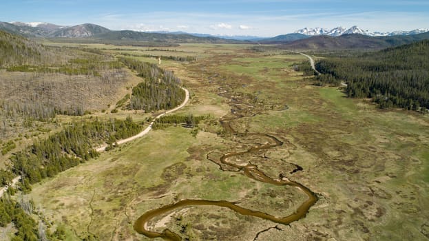 A breathtaking aerial view of a tranquil valley featuring a winding river, lush greenery, and distant rocky mountains under a clear blue sky in Stanley, Idaho.
