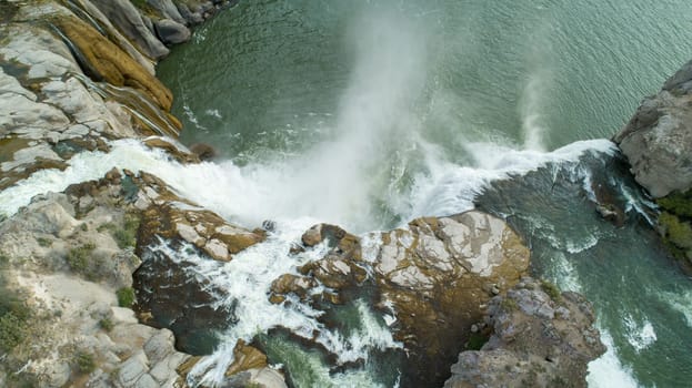 Captivating aerial view of a powerful waterfall cascading over rugged rocks into a serene body of water, surrounded by natural beauty at shoshone falls in twin falls