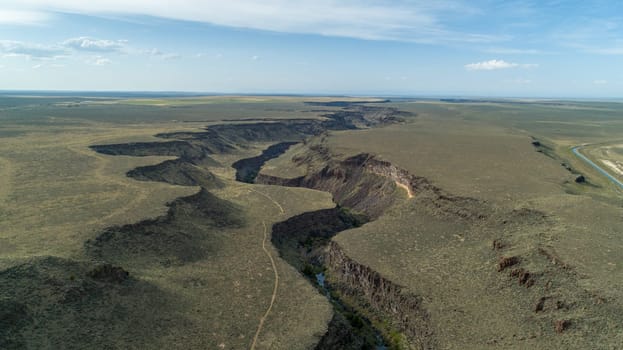 Expansive aerial view of a dramatic canyon landscape with rugged terrain and a winding path under a clear blue sky, highlighting natural beauty and adventure potential.