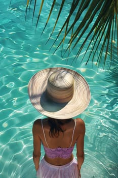 A female wearing a hat is positioned in a body of liquid, surrounded by azure water. She enjoys leisure time in the pool with aquatic organisms and plants