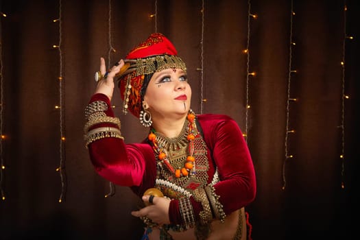 A woman in a colorful headscarf and jewelry poses in front of wall of colorful tassels