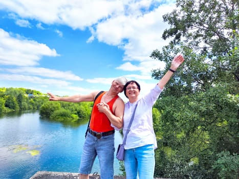 couple enjoys a cheerful moment together, holding hands at the river's edge surrounded by lush greenery and bright skies