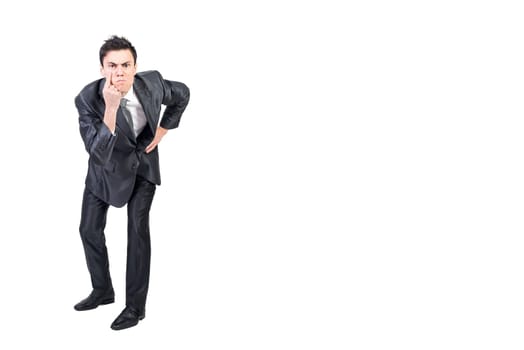 Full body of serious young male manager with dark hair in formal suit pointing at eye and gazing at camera while standing against white background with hand on waist