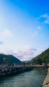 A large group of boats are floating on a lake. The sky is blue with some clouds