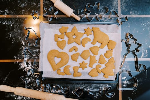 Tray of baked gingerbread cookies sits on the table next to the cookie cutters. Top view. High quality photo