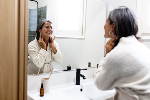 Mature happy woman looking herself in bathroom mirror smiling.Wellness and lifestyle concept.