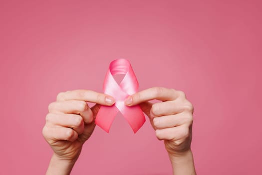 Woman holding pink ribbon on pink background, close up. Breast cancer awareness concept,