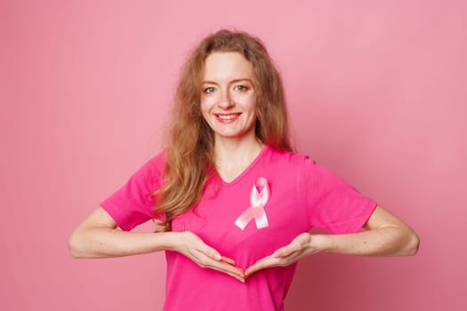 Close up of smiling young woman with pink ribbon pinned to her shirt symbolizing breast cancer awareness and importance of early detection. Healthcare concept