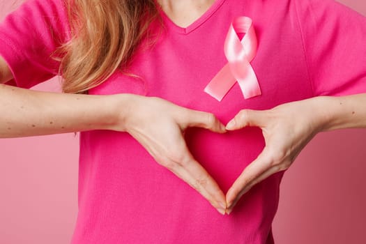 Young woman with pink ribbon making heart gesture on color background. Breast cancer awareness concept
