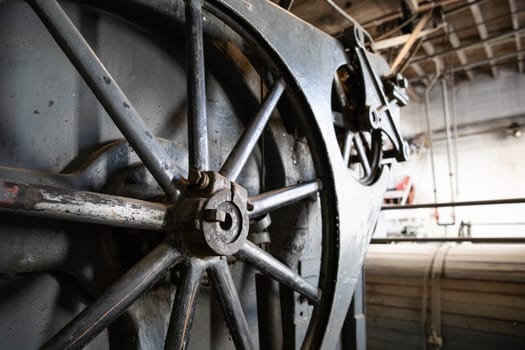Detailed view of a large industrial machine wheel within a factory environment, highlighting the intricate metalwork and engineering. Emphasizes industrialization and the robust nature of machinery.