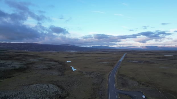 Iceland. A road cuts through a dry, barren landscape. The sky is cloudy and the sun is setting