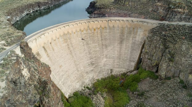 Stunning aerial photograph showcasing a massive concrete dam nestled within a rugged canyon landscape, surrounded by natural beauty. Highlights architectural strength and environmental harmony.