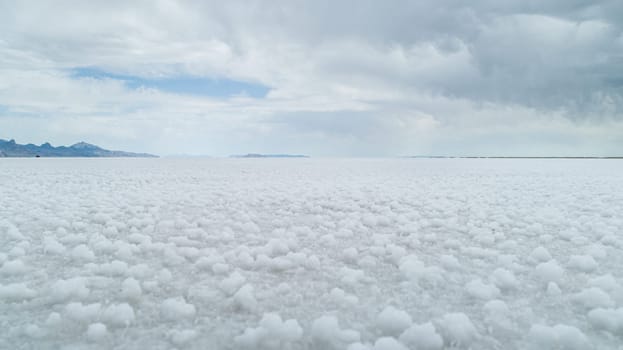 A wide view of expansive white salt flats under a cloudy sky, with distant mountains visible on the horizon, creating a serene and tranquil landscape.