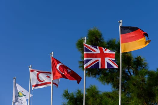 Flags representing Germany, the UK, and Turkey wave gracefully against a sunny backdrop of nature.