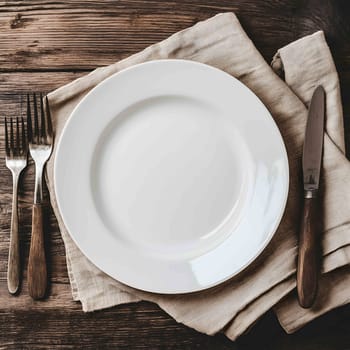 Empty white plate is waiting on a rustic wooden table with silverware on a napkin