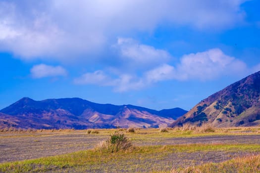A picturesque landscape of rolling hills with vibrant green grass under a dramatic blue sky and fluffy white clouds.