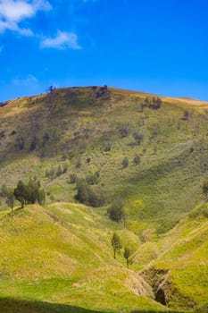 A picturesque landscape of rolling hills with vibrant green grass under a dramatic blue sky and fluffy white clouds.