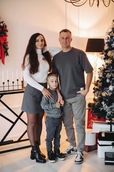 Happy family mom dad son at the Christmas tree on Christmas day.