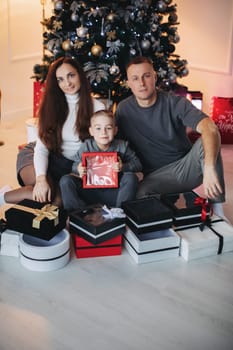 Happy family mom dad son at the Christmas tree on Christmas day.