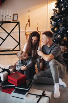 Happy family mom dad son at the Christmas tree on Christmas day.