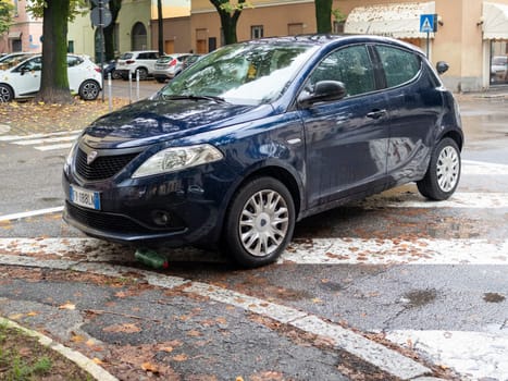 Cremona, Lombardy, Italy October 15th 2024 Dark blue lancia ypsilon improperly parked on pedestrian crossing with a plastic bottle underneath the front bumper on a rainy autumnal day