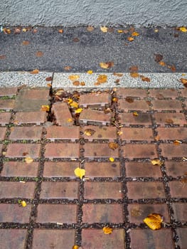 Cremona, Lombardy, Italy October 15th 2024 Damaged sidewalk with missing and broken red bricks, scattered autumn leaves, and cigarette butts, indicating neglect and urban decay