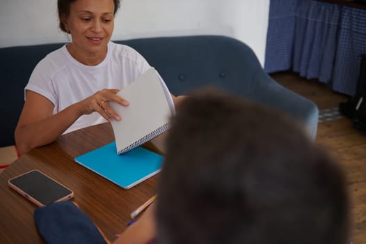 A woman sits across a wooden table sharing ideas with a colleague in a relaxed, informal meeting. She's flipping through notes, and a smartphone lies nearby, creating a collaborative atmosphere.