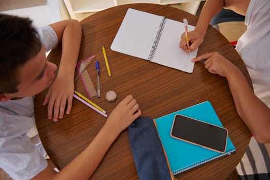 Two students work together on a homework project, using notebooks and pencils at a round table, emphasizing collaboration and learning.