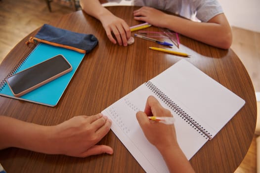 Two students collaborate on a study project at a round wooden table, with notebooks, pens, and a smartphone scattered around. They focus on learning and homework tasks, emphasizing teamwork.